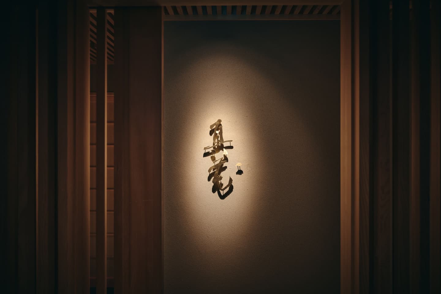 スポットライトに照らされ壁面に美しい影を落とす高級和食店のロゴ看板、空間のアイデンティティを象徴する静謐なインテリア撮影