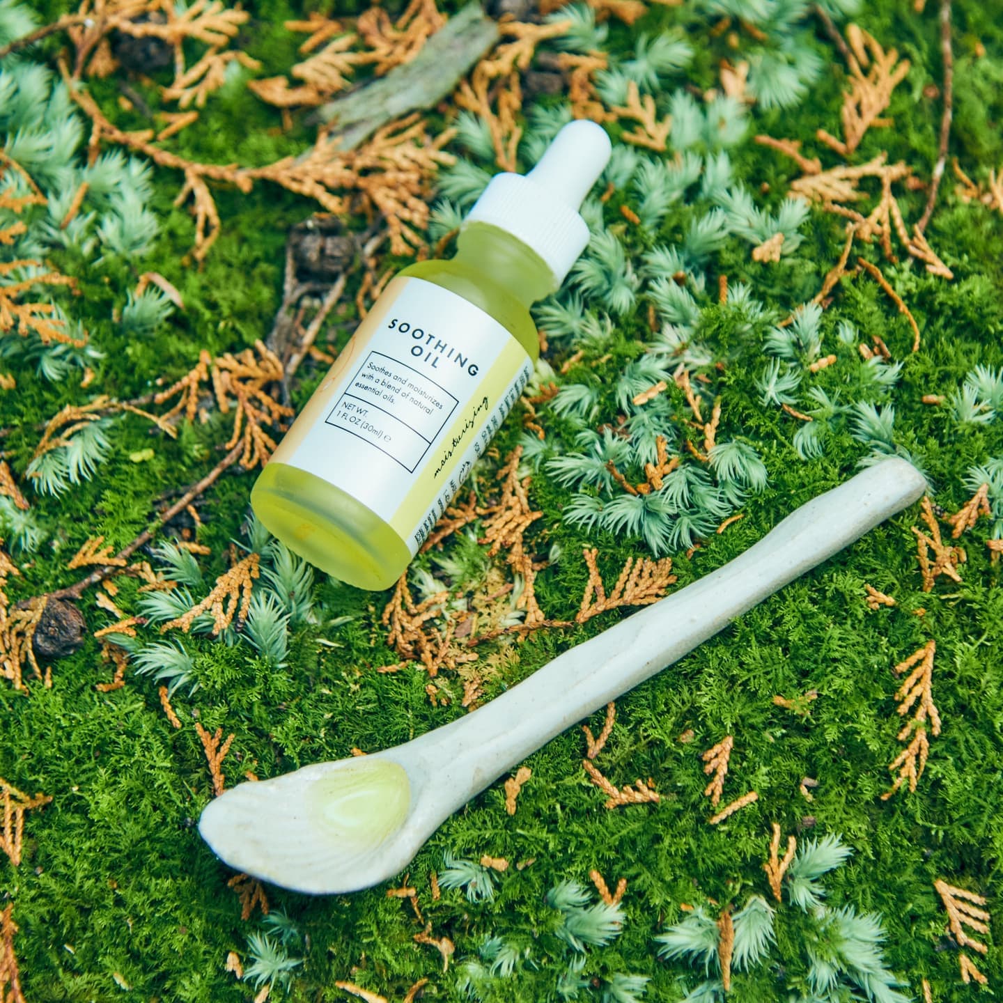 苔の上に置かれたオーガニックオイルのボトル。人物と共通のトーンで撮影されたD2Cブランド向けプロダクトビジュアル。