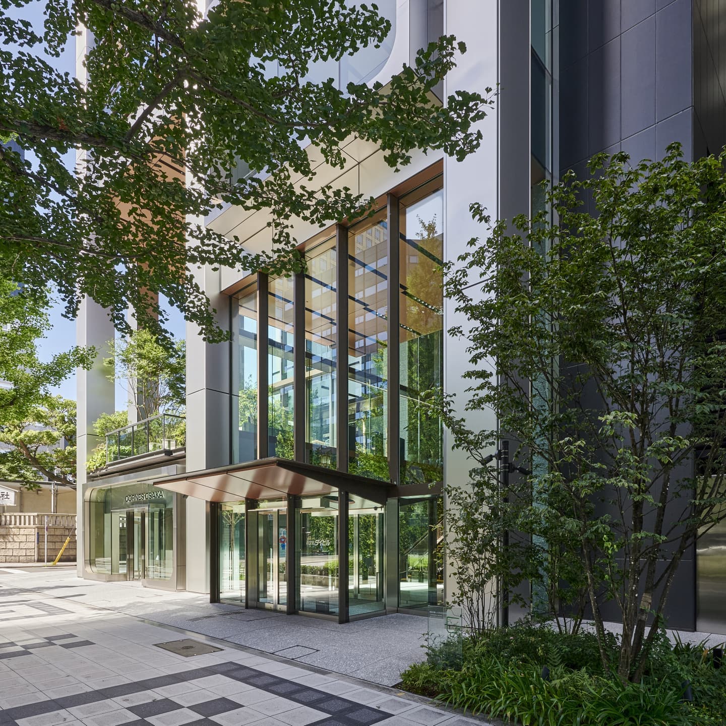 大阪のオフィスビル・商業施設のエントランス竣工写真。植栽とガラスカーテンウォールが調和する外観撮影。