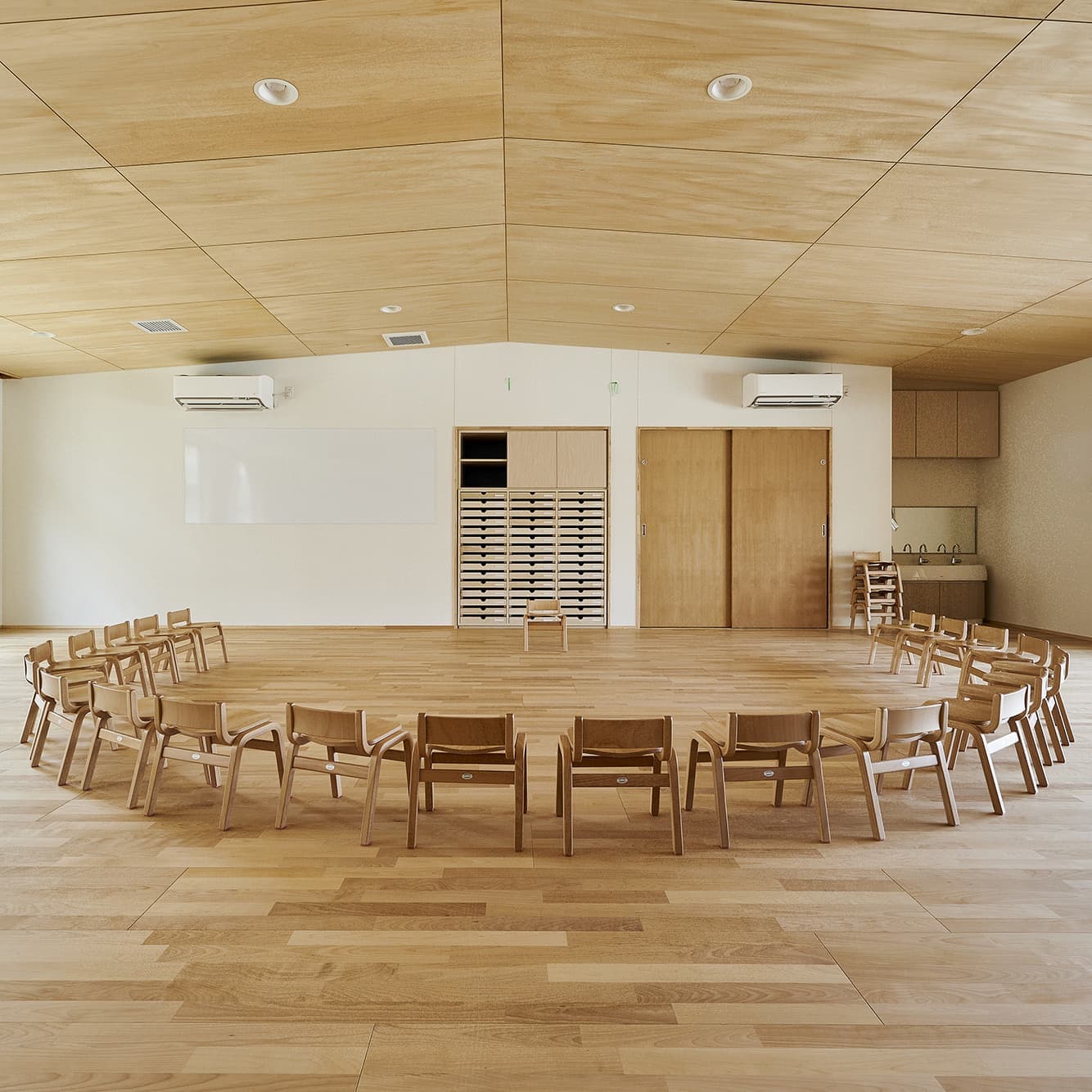 木質空間の内観竣工写真。園舎や施設の温かみを伝える、円状に配置された椅子と柔らかな自然光による空間演出。