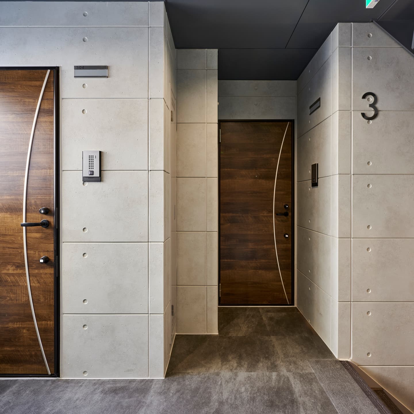 マンション共用部の玄関ドアとインターホン周りの撮影事例。コンクリート打ち放しのモダンな質感と、ドアノブや建具のエッジまでシャープに表現した内覧写真。