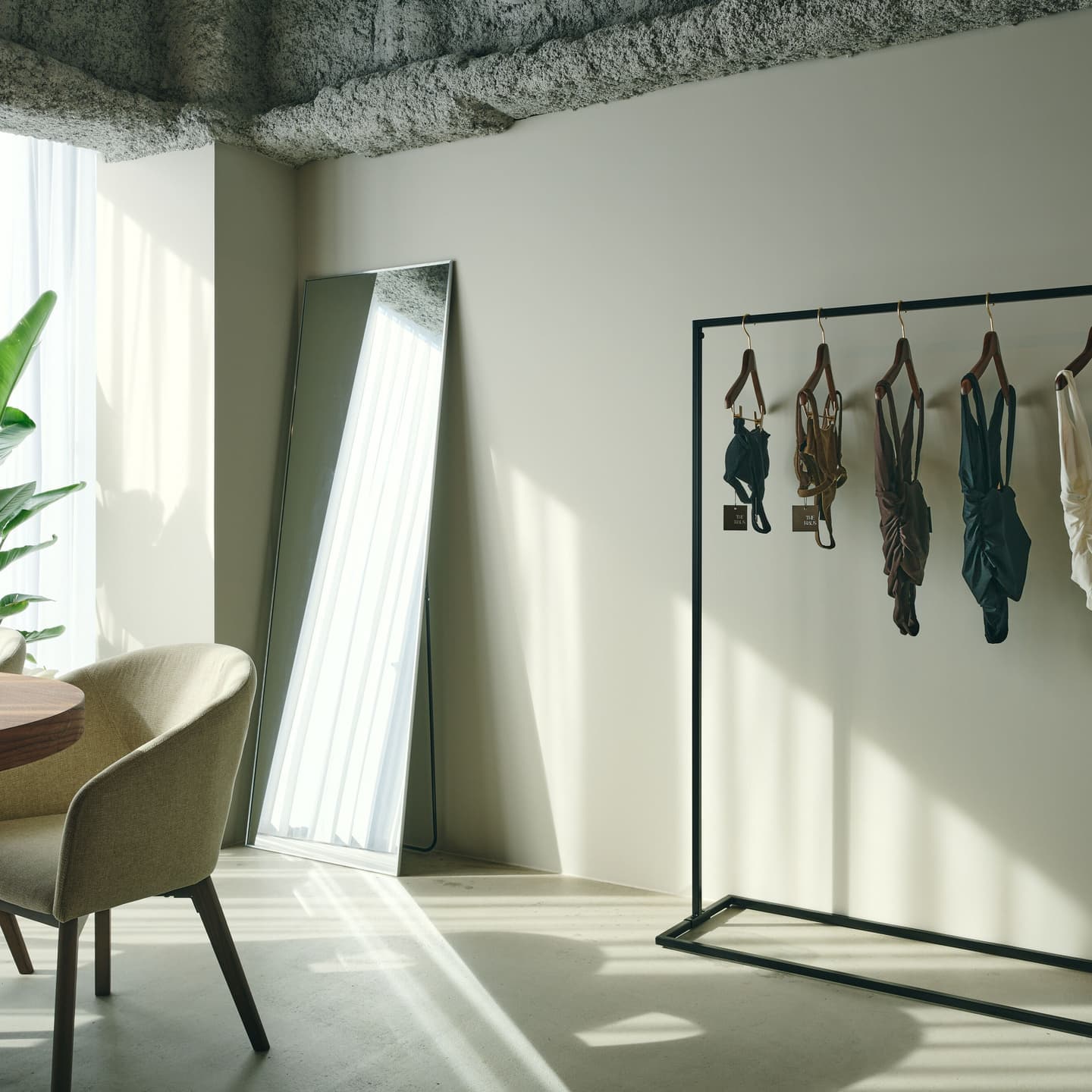 セレクトショップ・サロンの内装イメージ。ハンガーラックに並ぶプロダクトと、窓から差し込む自然光が作り出す光と影のコントラストを美しく捉えた空間写真。