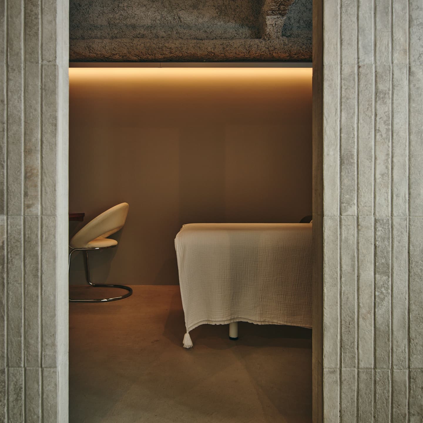 プライベートサロンの内装ディテール。質感のある壁面の間から覗く施術ルームの風景。没入感とプライバシーを両立させた空間デザインの竣工写真。