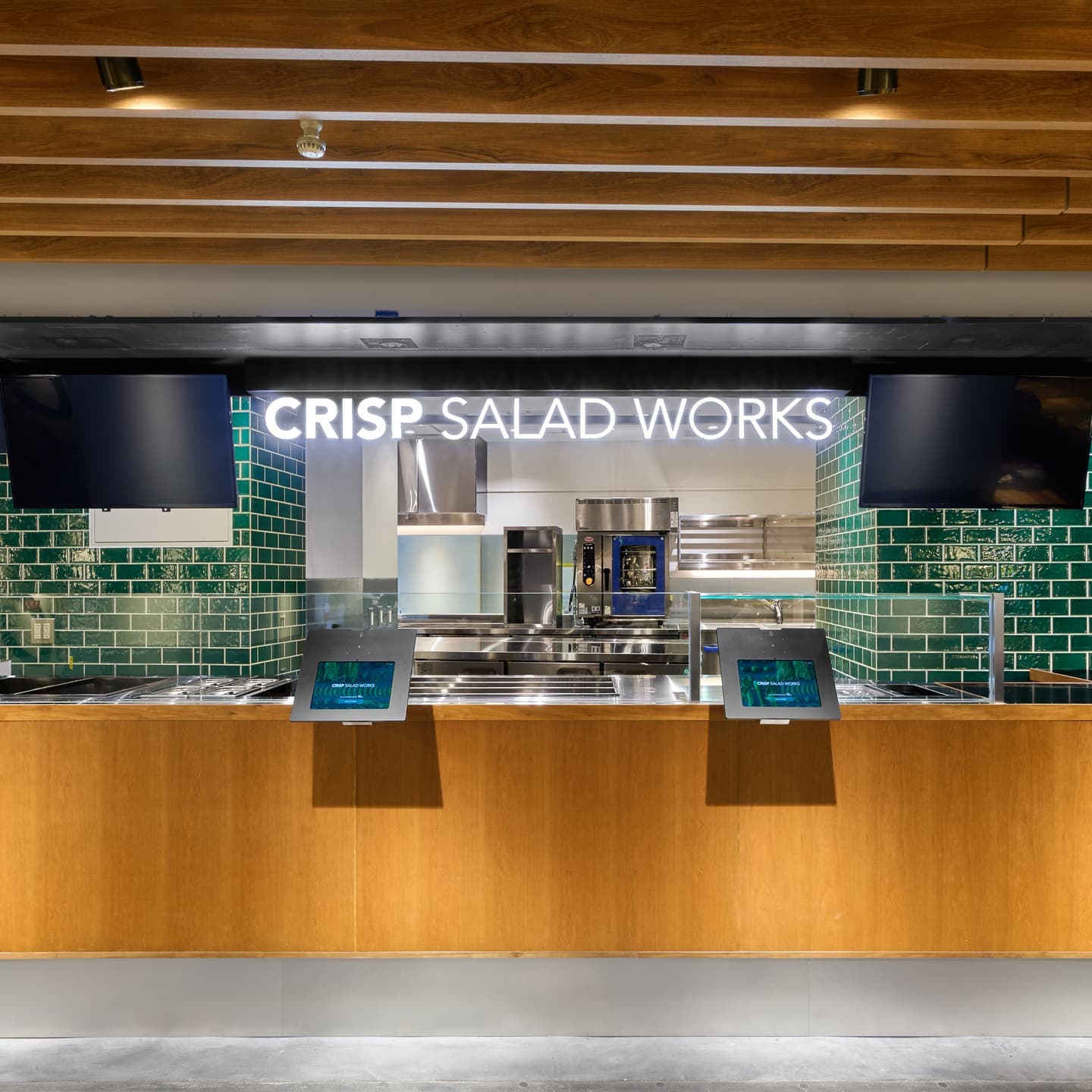 落ち着いた木目のカウンターと鮮やかなグリーンのタイルが特徴的な、CRISP SALAD WORKSのモダンでクリーンな店舗外観。