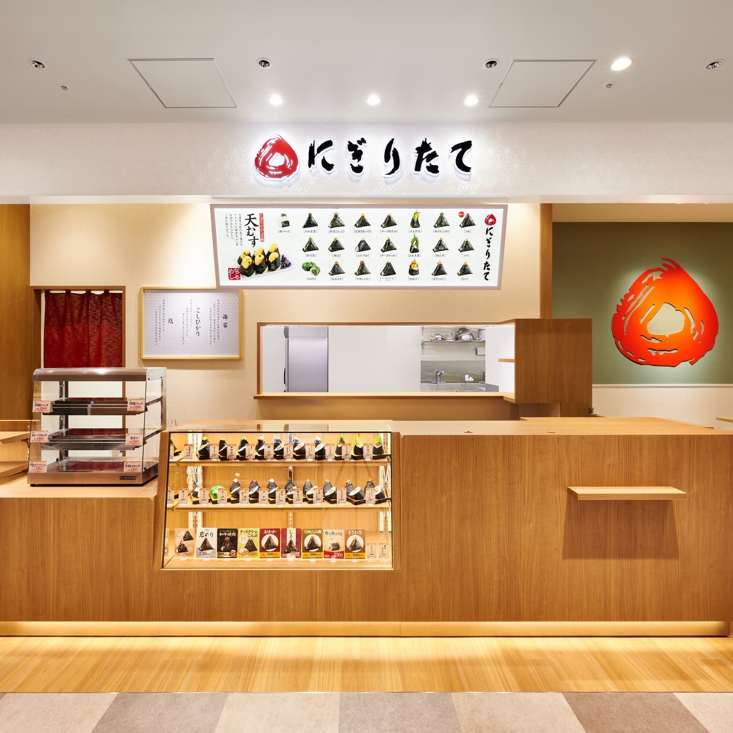 温かみのある明るい木材を基調とした「にぎりたて」の店頭。ショーケースに整然と並ぶおむすびと、和の柔らかいライティングが調和した空間。