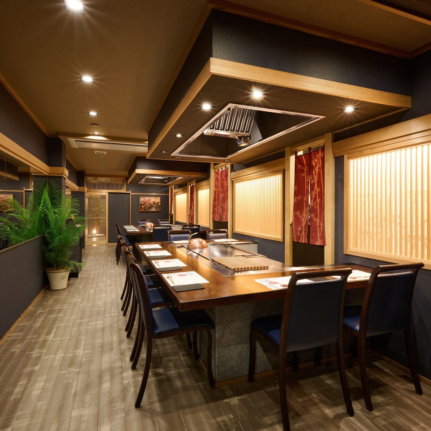 重厚感のあるダークトーンの壁面と木製格子が織りなす、洗練された鉄板焼き店の内装。整えられたカウンター席と落ち着いた間接照明による上質な空間。